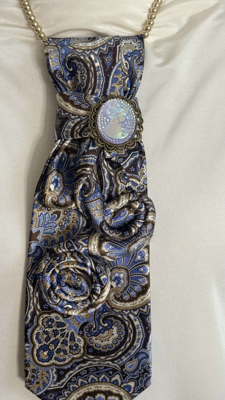 Blue and gold paisley necktie gathered into folds with an opal cabochon brooch, on a gold chain.