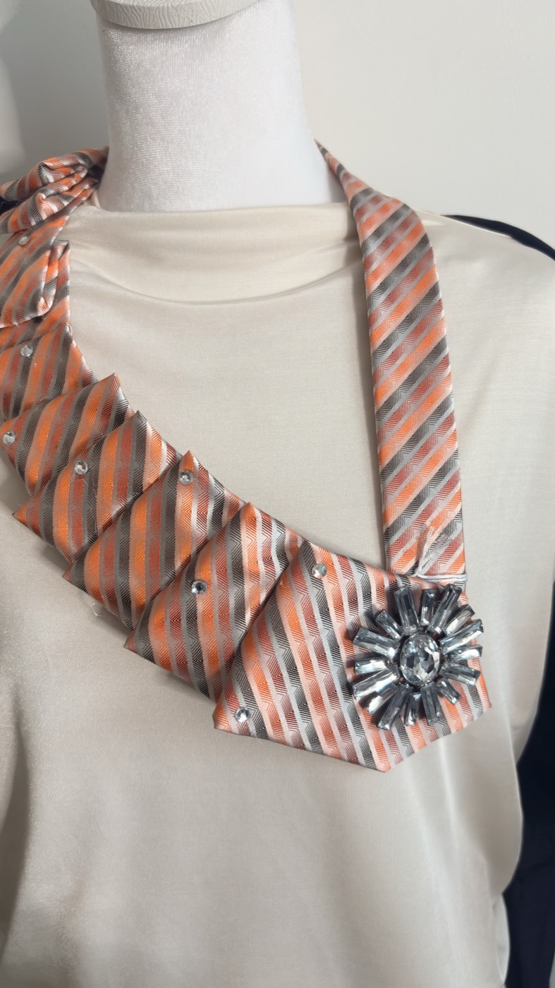 Orange, grey and white striped necktie pleated on one side with a large crystal sunburst brooch.